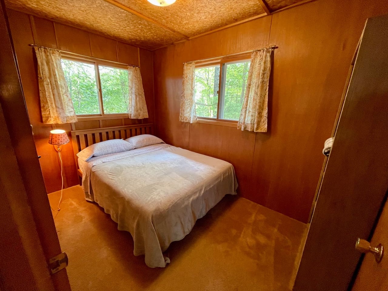 Sink into your cozy wood-paneled bedroom where soft lamplight and forest views create your perfect retreat.