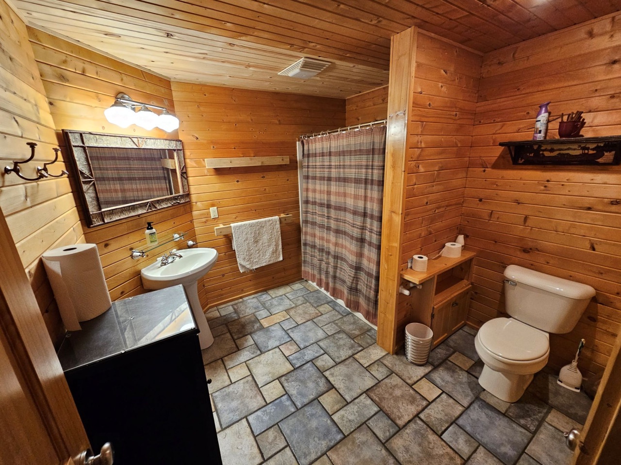 Step into your rustic cabin bathroom where warm wood walls and charming plaid accents create a cozy retreat for refreshing after your mountain adventures.