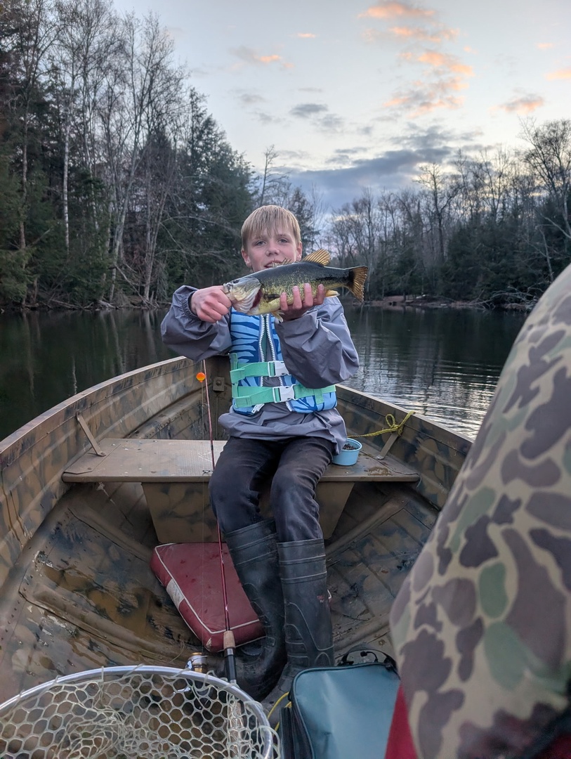 A young angler proudly displays a fresh catch from a peaceful lakeside fishing adventure, surrounded by quiet waters and wooded shores.