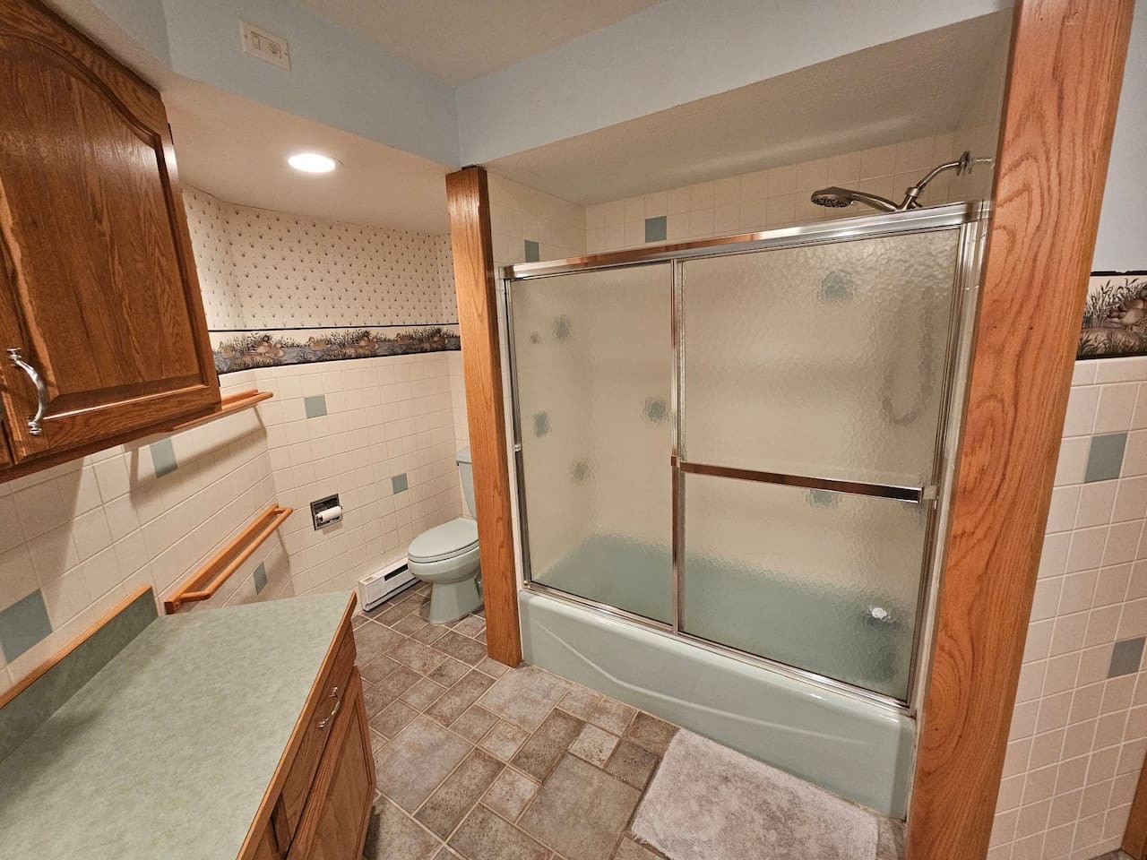Step into your private bathroom featuring warm wood accents and a relaxing tub-shower combo with glass doors for your comfort.