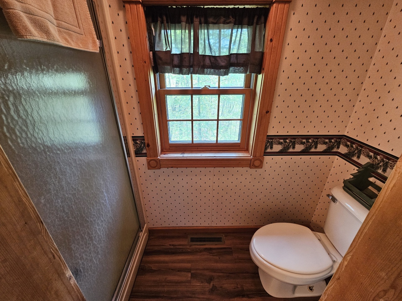 Your charming bathroom features classic wood floors, vintage wallpaper, and a bright window that fills the space with natural light.