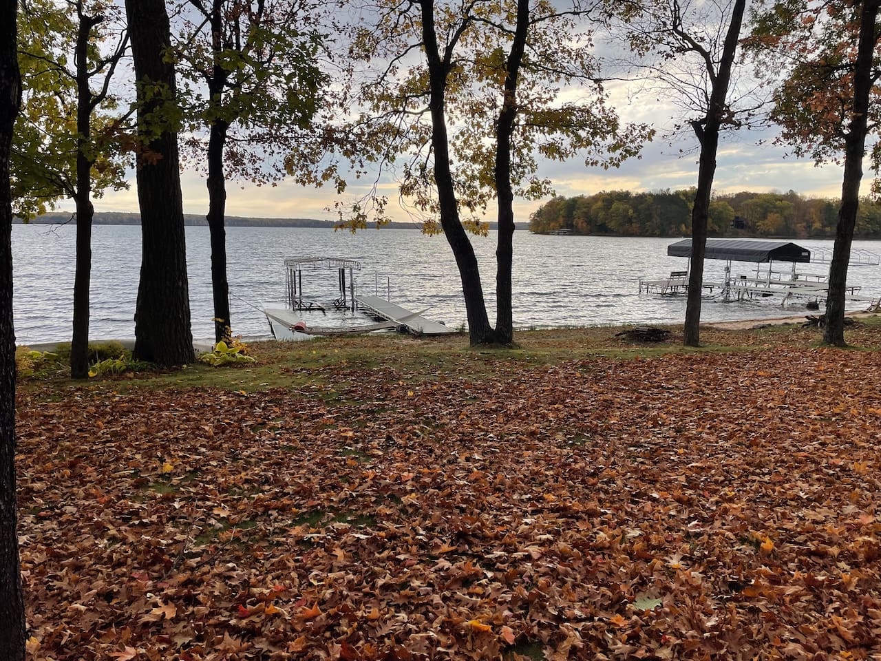 Peaceful lakefront setting with autumn foliage and private dock access surrounded by mature trees and calm waters.