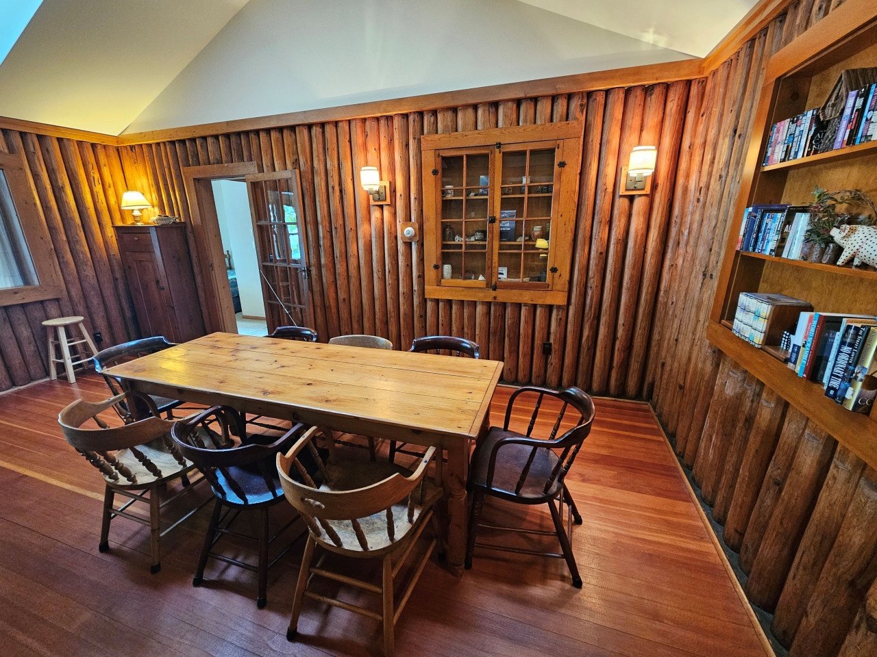 Gather around this rustic wooden table surrounded by warm paneling and shelves of books, creating your perfect space for meals and conversations.