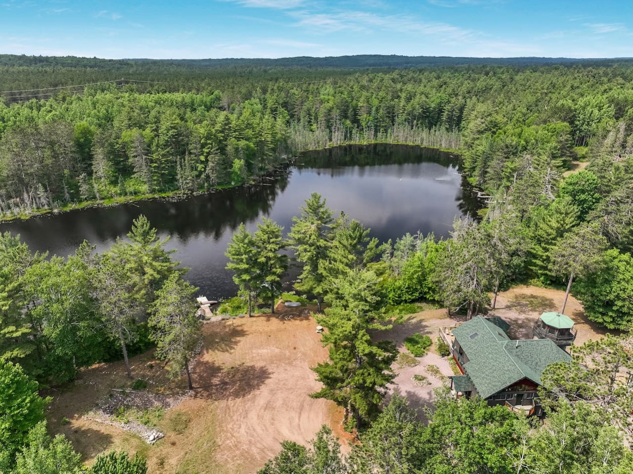 Aerial view of a secluded lakefront property nestled among pristine forests, featuring a private lake surrounded by towering pines and natural wilderness.
