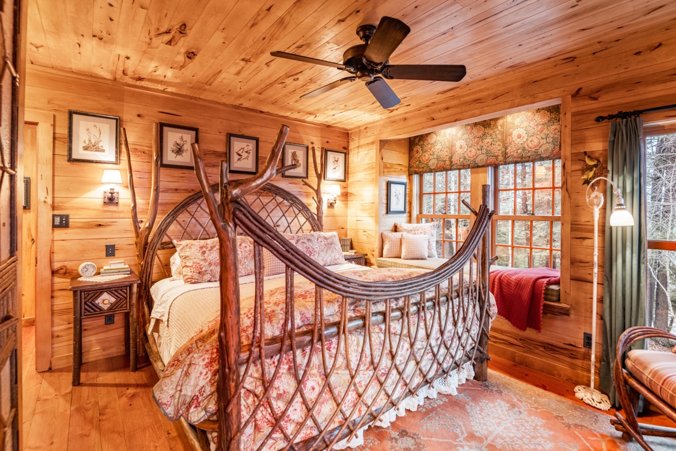 Step into your rustic cabin bedroom where warm wood surrounds you and a unique wrought iron bed promises cozy nights under the ceiling fan.