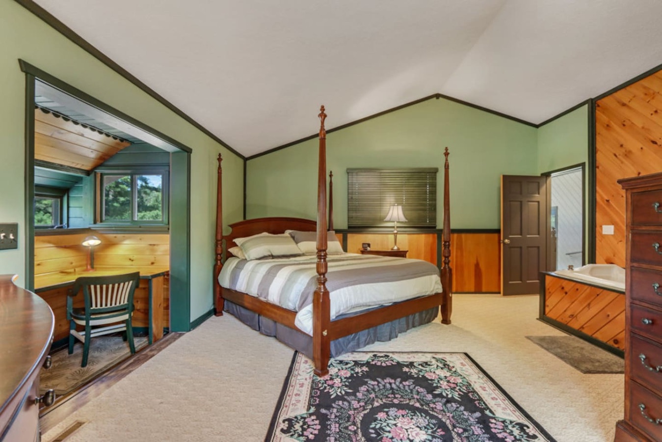 Your elegant four-poster bed awaits in this spacious bedroom, where warm wood accents and soothing green walls create the perfect retreat.