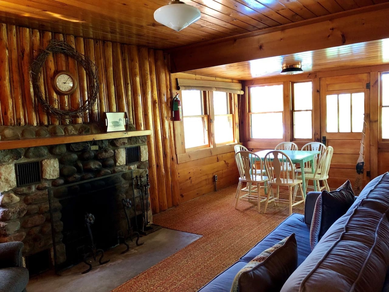 Cozy up by the stone fireplace in this rustic log cabin retreat, where warm wood surrounds you and natural light streams through picture windows.