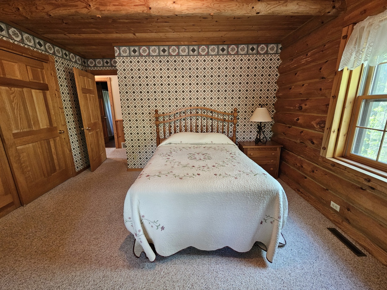 Drift off in this charming rustic bedroom featuring handcrafted log walls, vintage-style wallpaper, and cozy quilted bedding for your perfect countryside retreat.