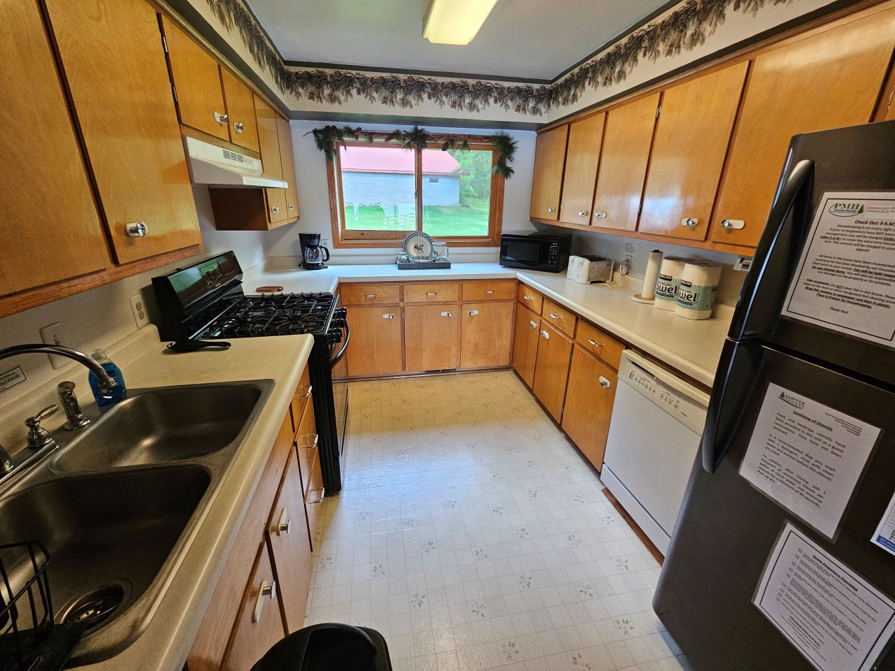 Your fully equipped kitchen features warm wood cabinets, modern appliances, and a charming window overlooking peaceful green surroundings.