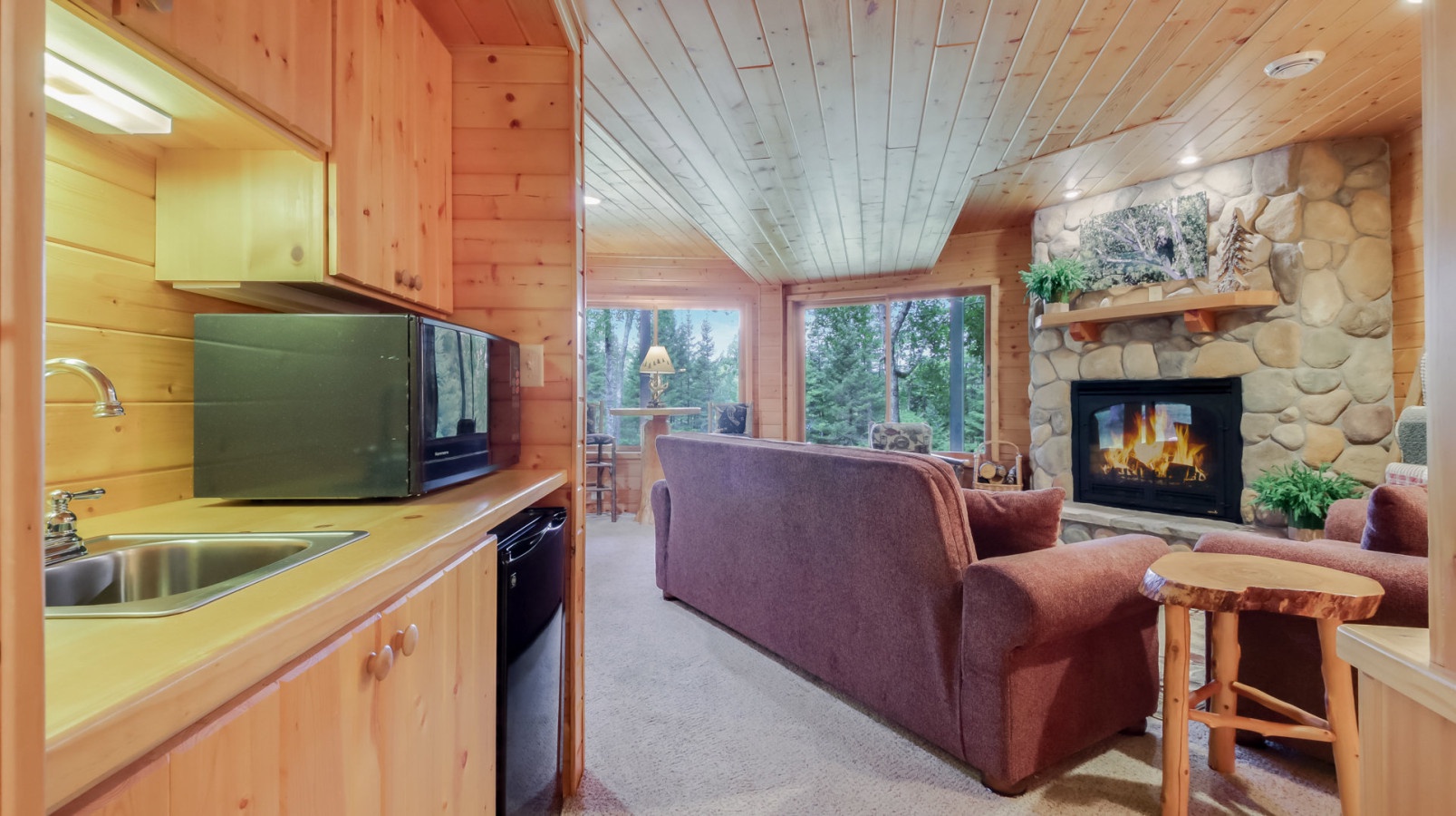 Cozy up by your stone fireplace while enjoying forest views from this warm wood-paneled living space with full kitchen.