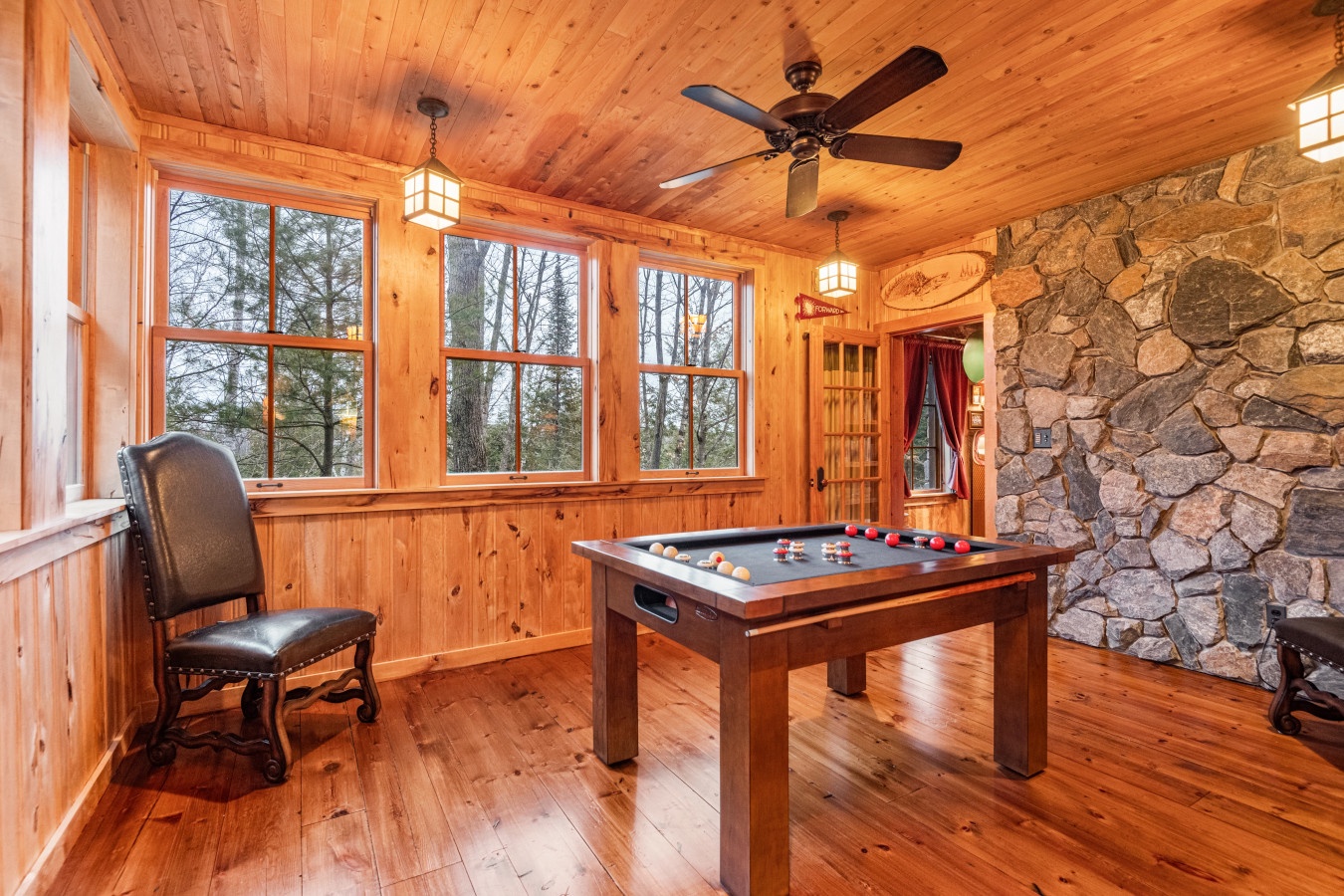Challenge friends to pool while enjoying forest views through expansive windows in this inviting wood-paneled game room.