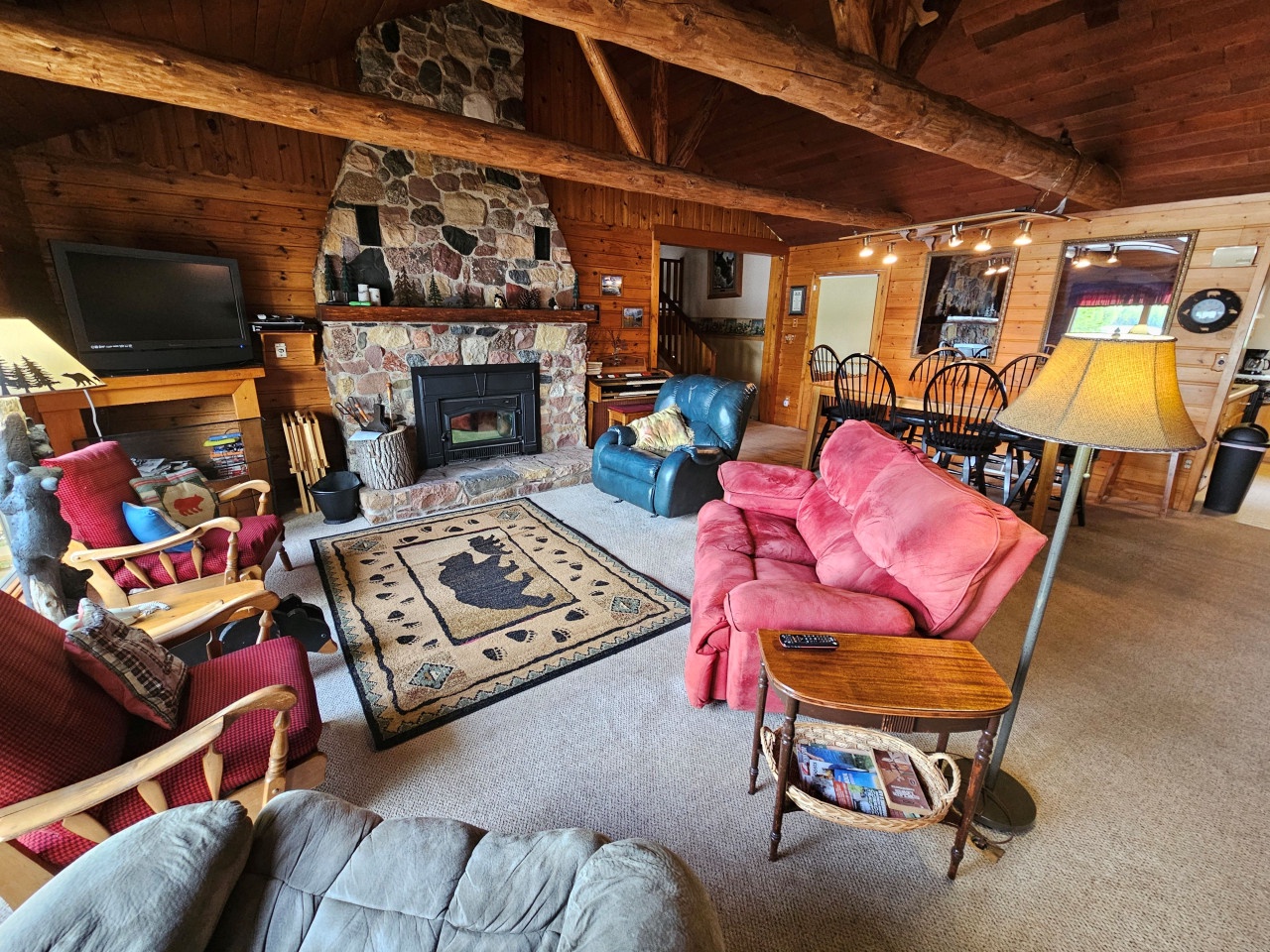 Gather around the stone fireplace in this cozy cabin living room, where rustic beams frame comfortable seating perfect for your evening relaxation.