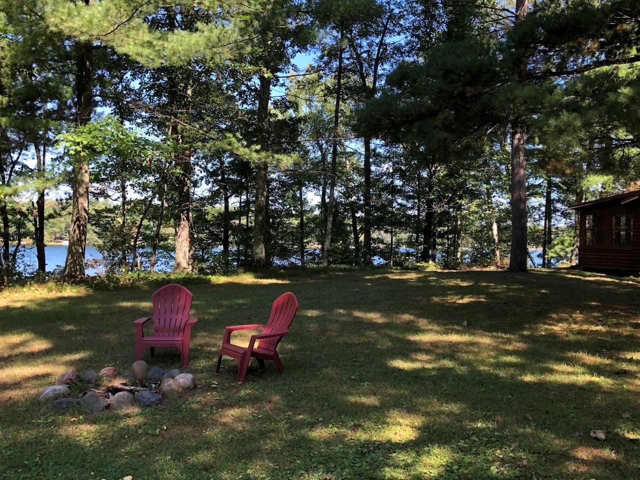 Relax in red Adirondack chairs by your private fire pit, surrounded by towering trees with glimpses of sparkling lake water through the forest.