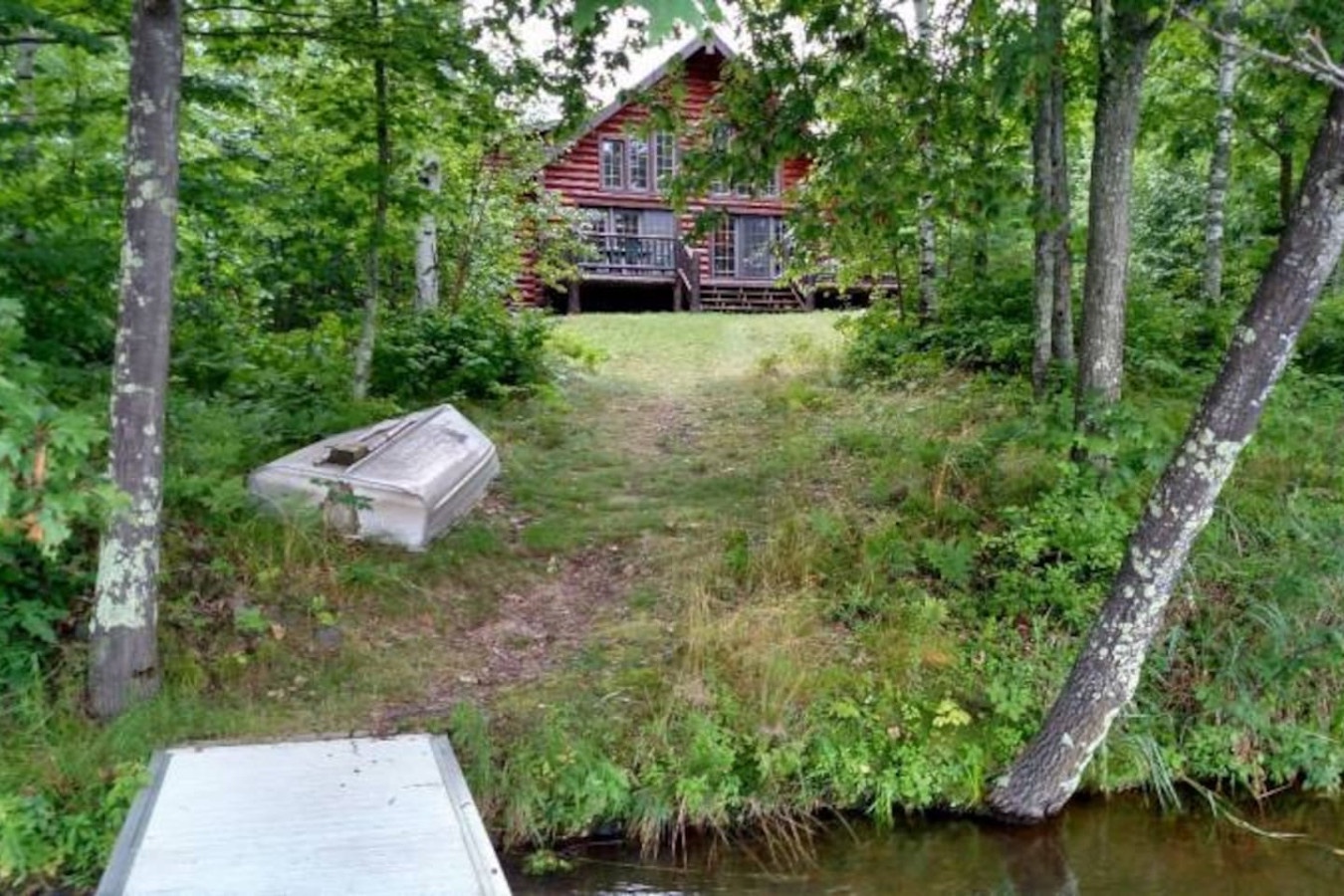 Rustic log cabin nestled among towering trees near peaceful waterfront with private dock access for fishing and water activities.