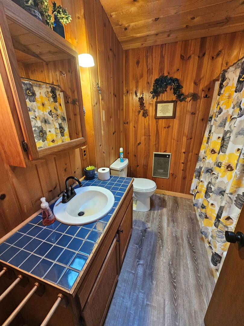 Step into your private rustic bathroom with warm wood walls, cheerful floral curtains, and blue tile accents that create a cozy cabin retreat.