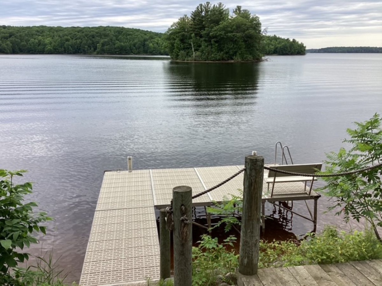 Tranquil lake with private dock extending into calm waters, surrounded by lush forested shoreline and peaceful natural beauty.