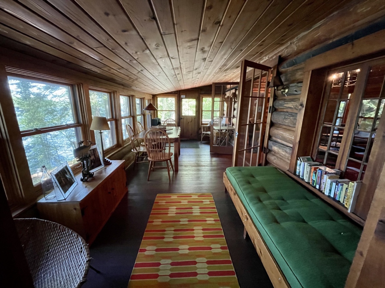 Curl up with a book on the cozy green daybed while enjoying stunning water views through floor-to-ceiling windows in this warm, wood-paneled retreat.