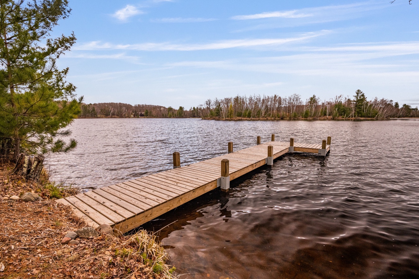 A serene lakefront dock surrounded by natural forest landscape with peaceful waters stretching to the wooded shoreline.