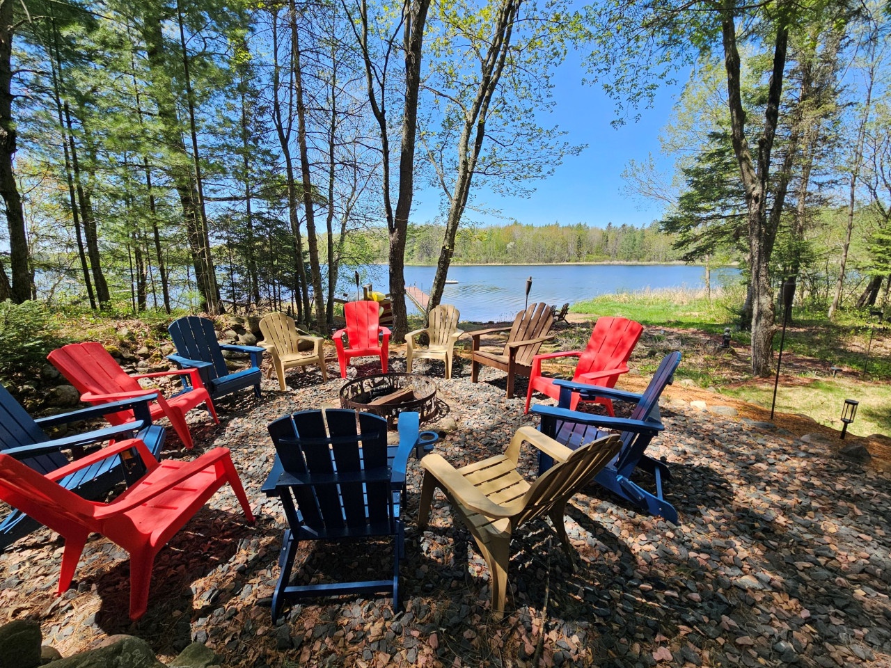 Gather around the colorful Adirondack chairs by your private fire pit, where evening conversations unfold under towering pines with peaceful lake views stretching beyond.