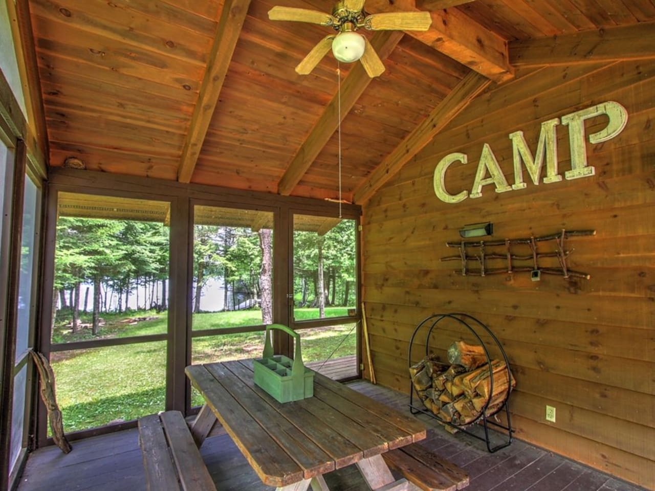 Relax in your private screened porch with exposed beams, fishing rods, and firewood ready for cozy camp adventures.