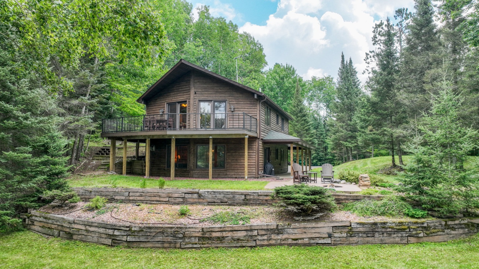 Rustic wooden cabin nestled among towering trees with wraparound porch and stone-terraced landscaping.
