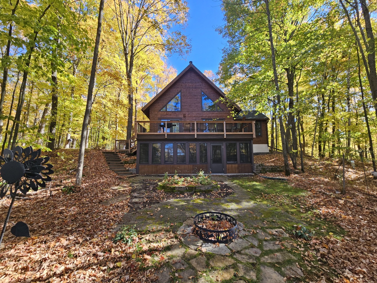 Charming forest cabin featuring a stone fire pit surrounded by golden autumn foliage and towering trees.