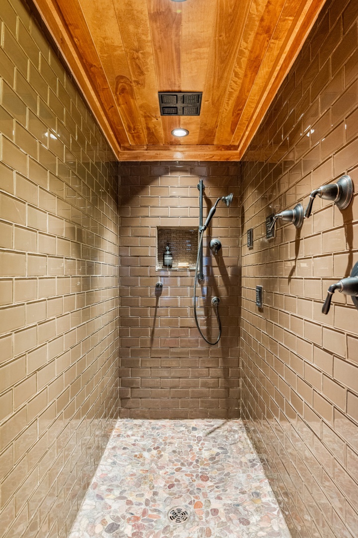 Step into your luxurious rainfall shower featuring warm subway tiles and rustic wood ceiling—your perfect retreat after exploring.