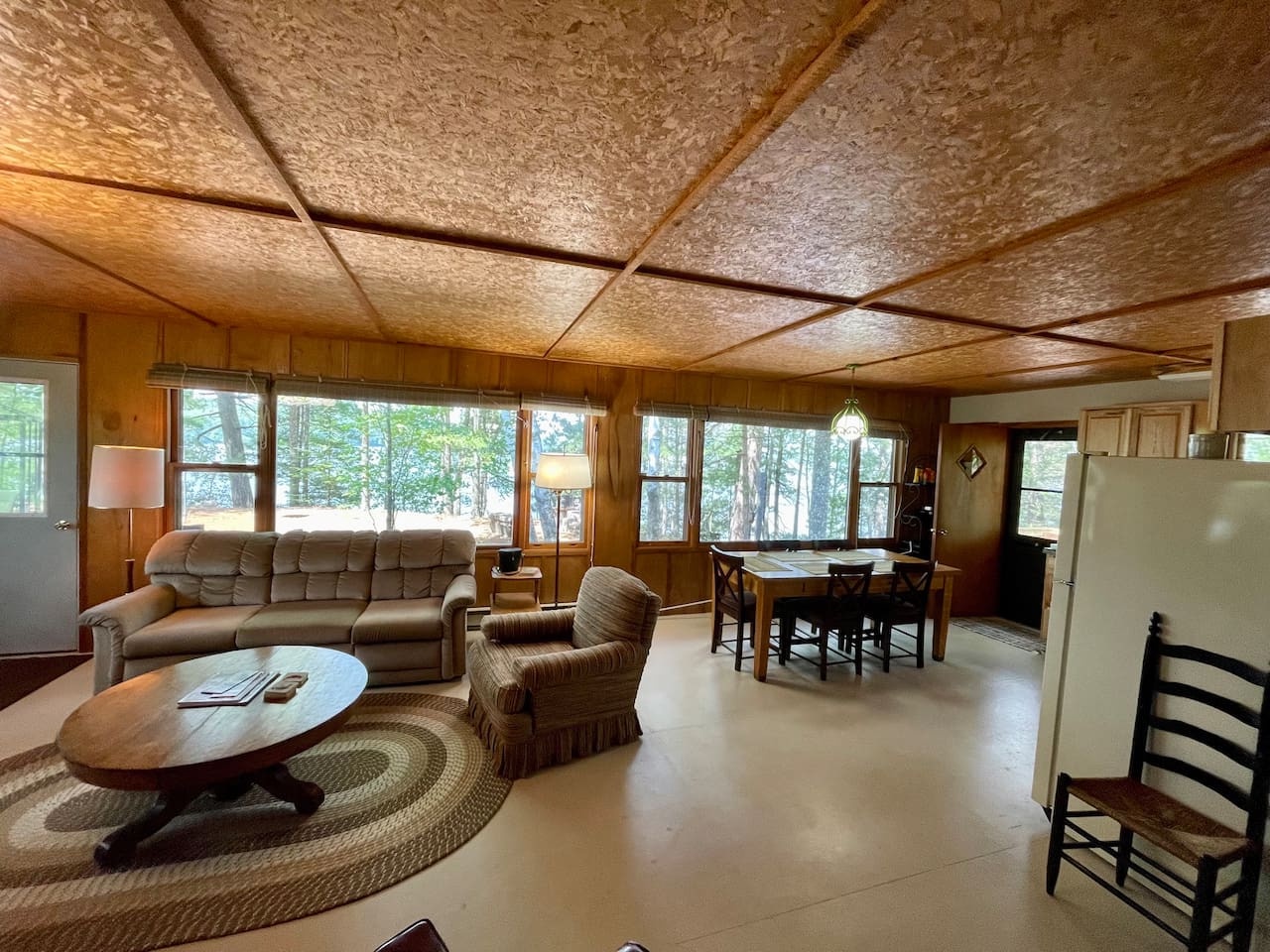 Relax in your spacious living room with comfortable seating, forest views through large windows, and an open layout perfect for gatherings.