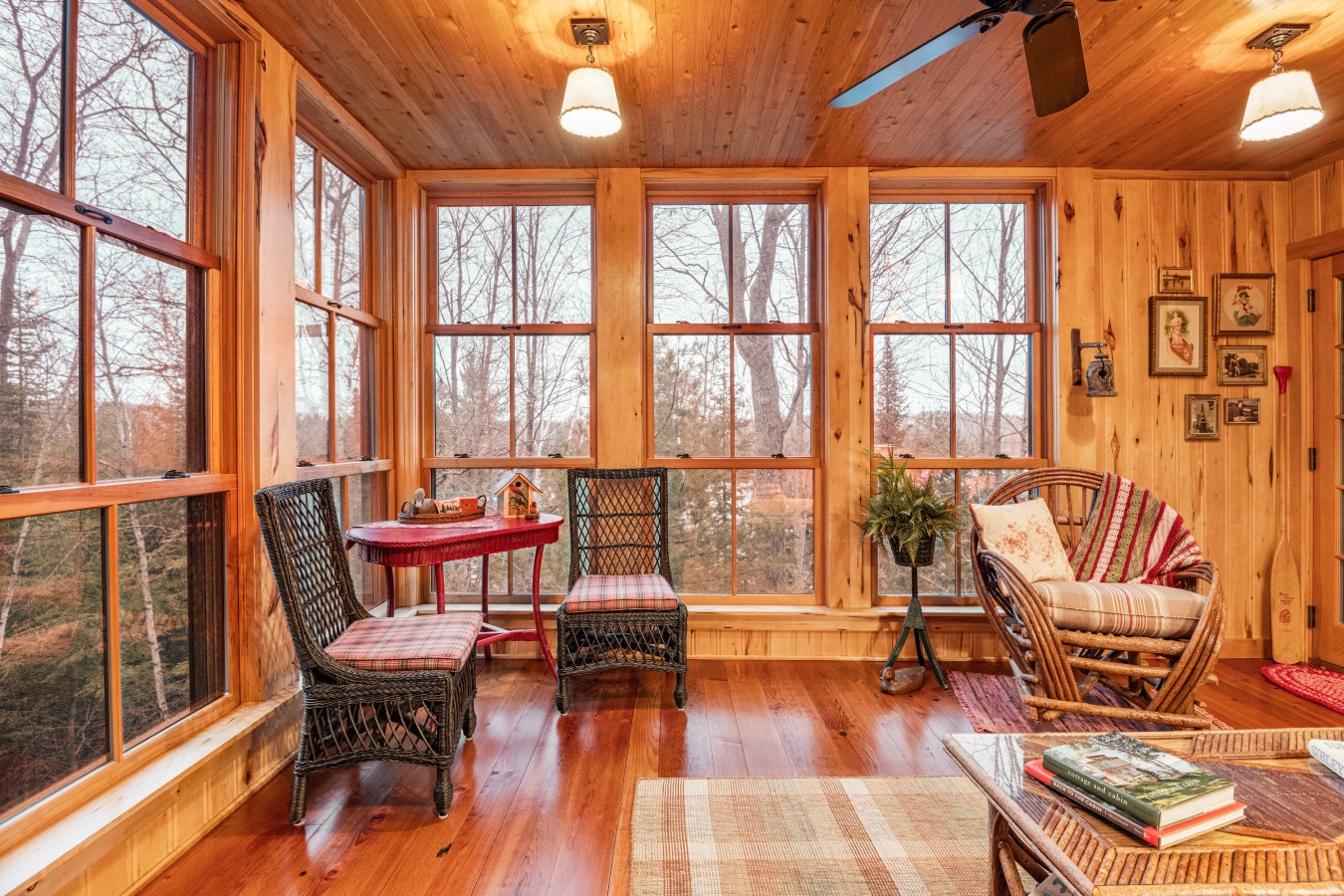 Cozy wood-paneled sunroom where you'll love reading by expansive windows overlooking peaceful winter trees, complete with rustic charm and comfy seating.