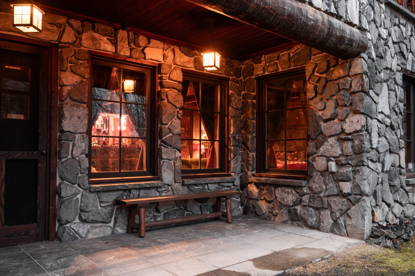 Stone lodge exterior with warm lighting glowing through windows creates a cozy mountain retreat atmosphere.