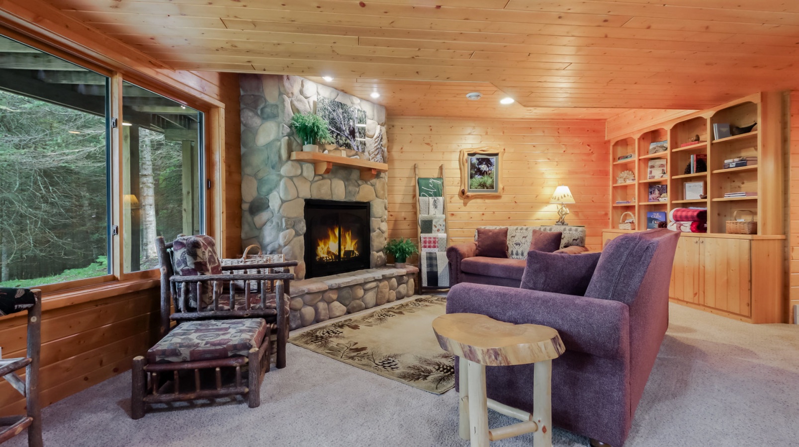 Cozy up in this warm wood-paneled living room where crackling fireplace flames and forest views create your perfect mountain retreat.