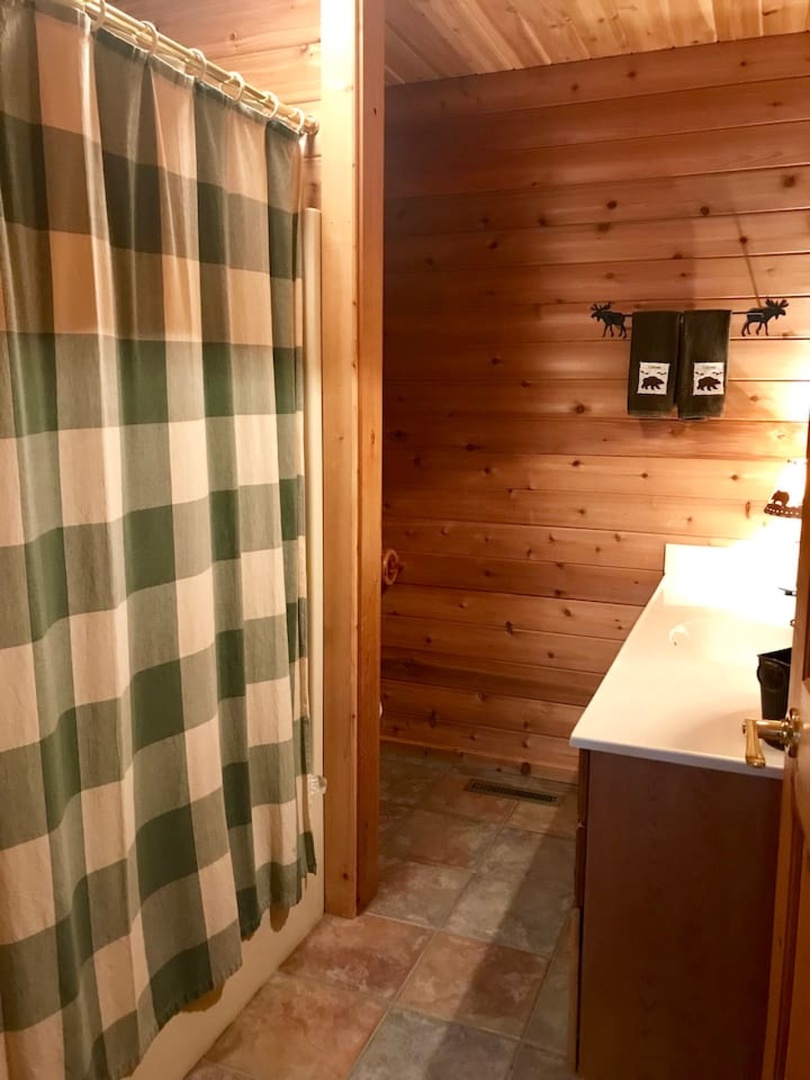 Your rustic bathroom features warm wood walls and charming wilderness-themed towels, creating a cozy cabin retreat feel.