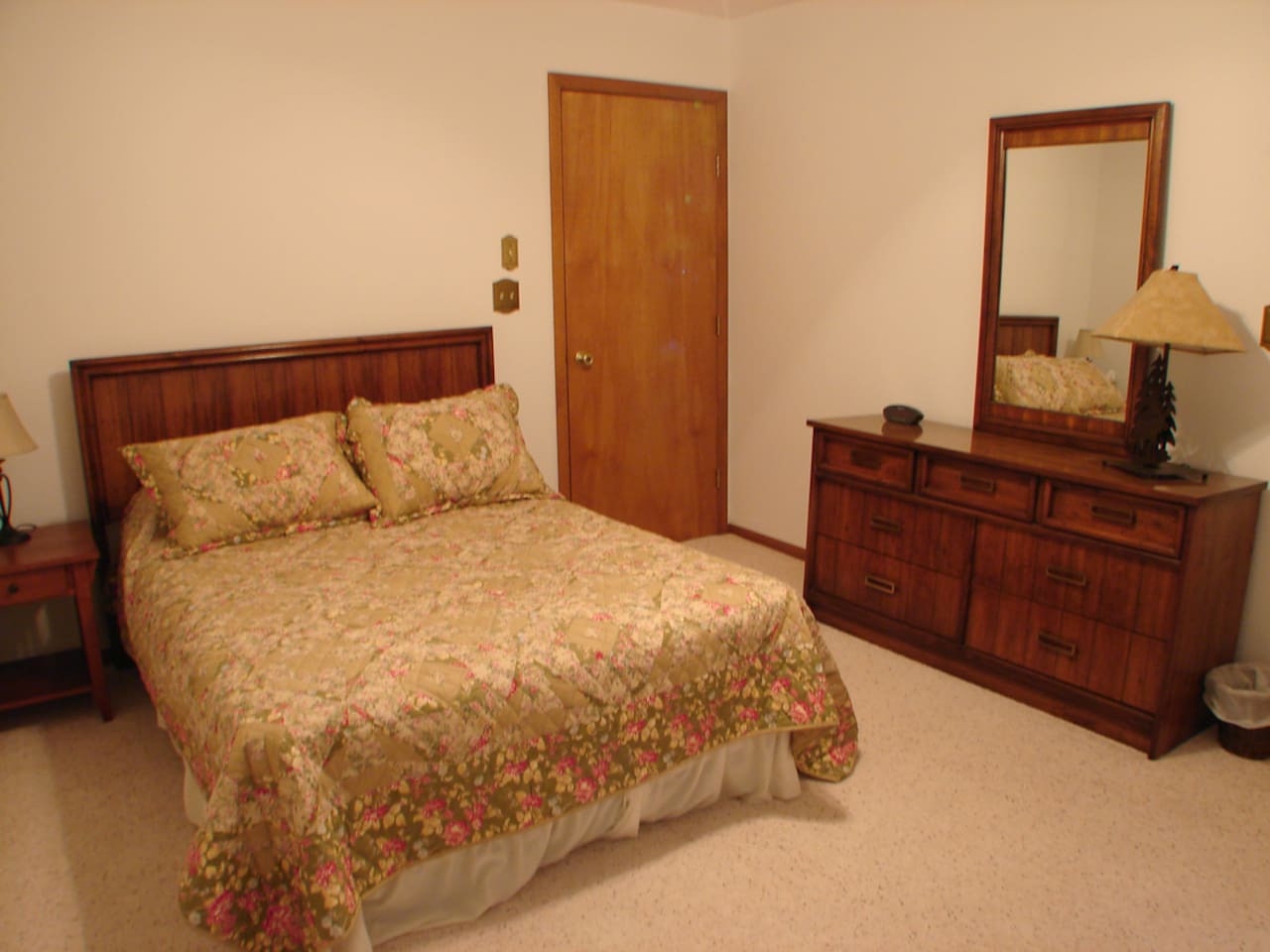 Relax in your serene bedroom featuring warm wood furnishings, a cozy floral-patterned bed, and thoughtful touches like bedside lighting for ultimate comfort.