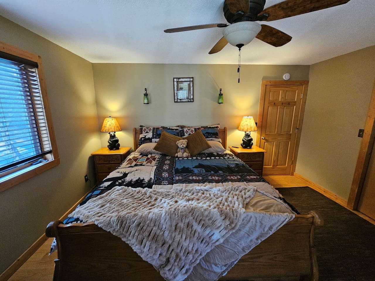 Drift off in this cozy bedroom featuring rustic charm with warm bedside lighting and a gentle ceiling fan for your comfort.