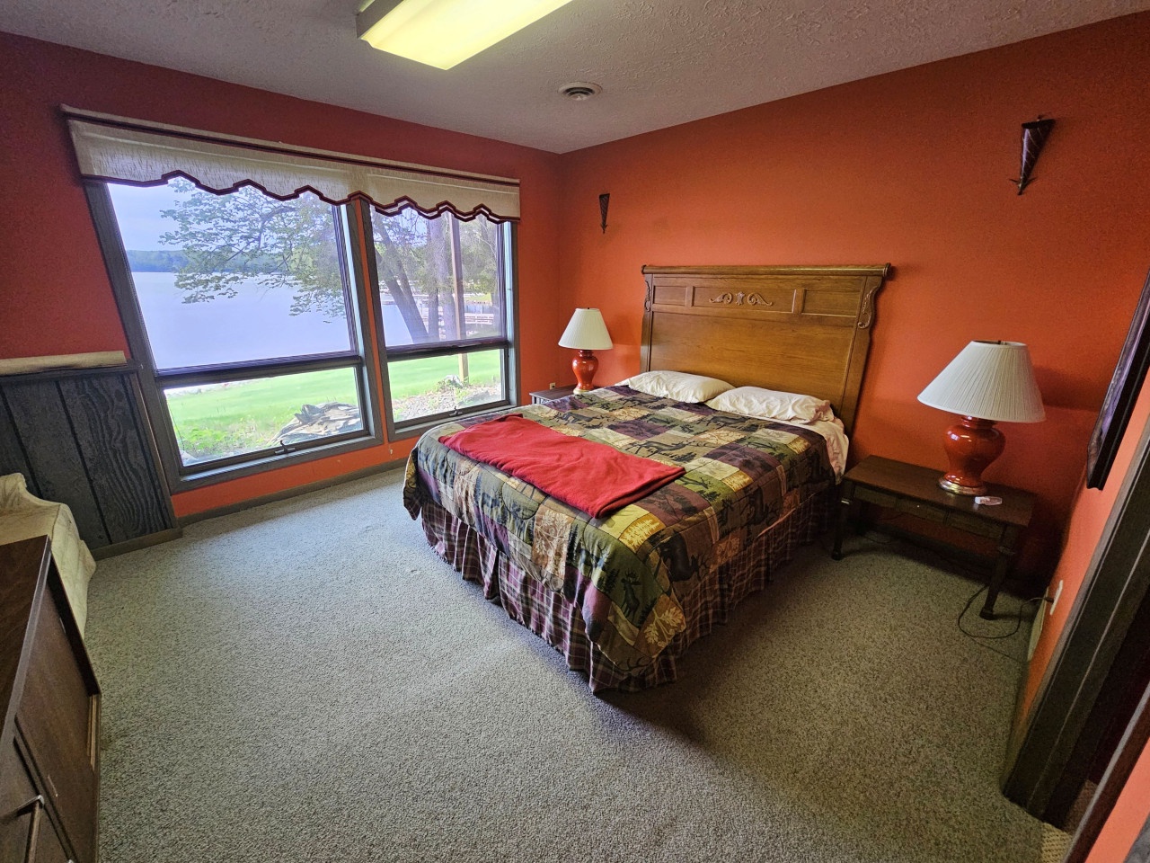 Wake up to peaceful lake views from your comfortable bedroom, where warm orange walls and rustic furnishings create a cozy retreat.