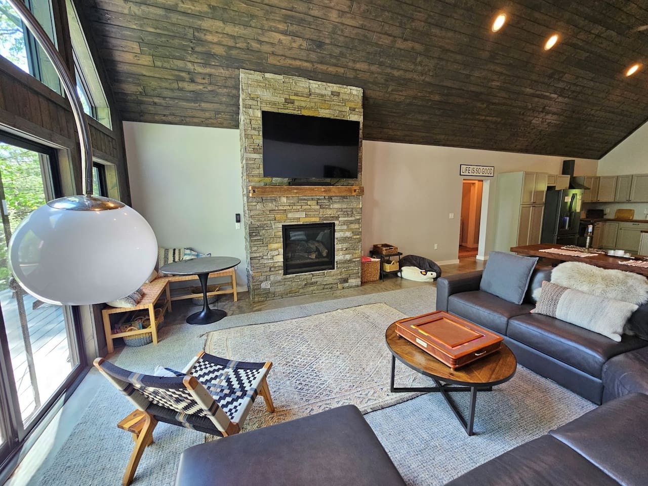 Unwind in your stylish living space featuring a cozy stone fireplace, modern furnishings, and panoramic windows overlooking nature.