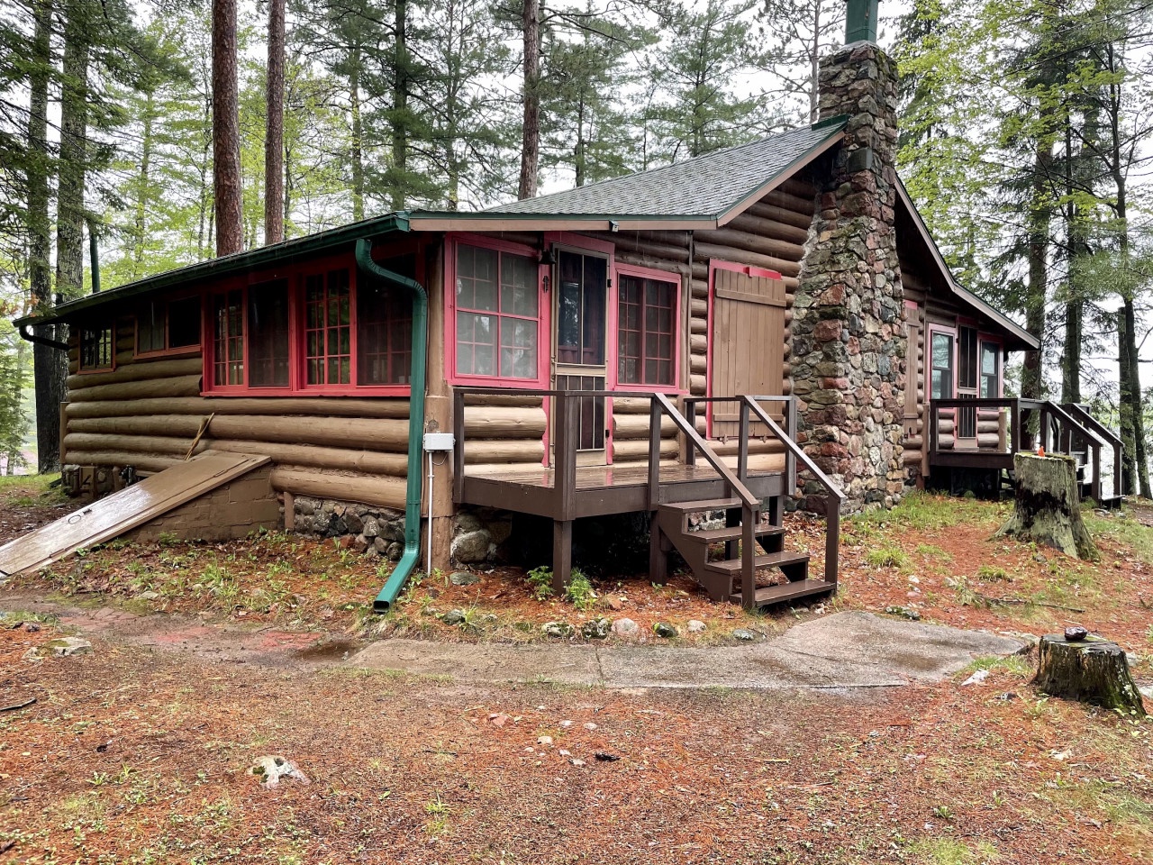 Charming log cabin nestled among towering pines with a stone chimney and welcoming front porch steps leading to your woodland retreat.