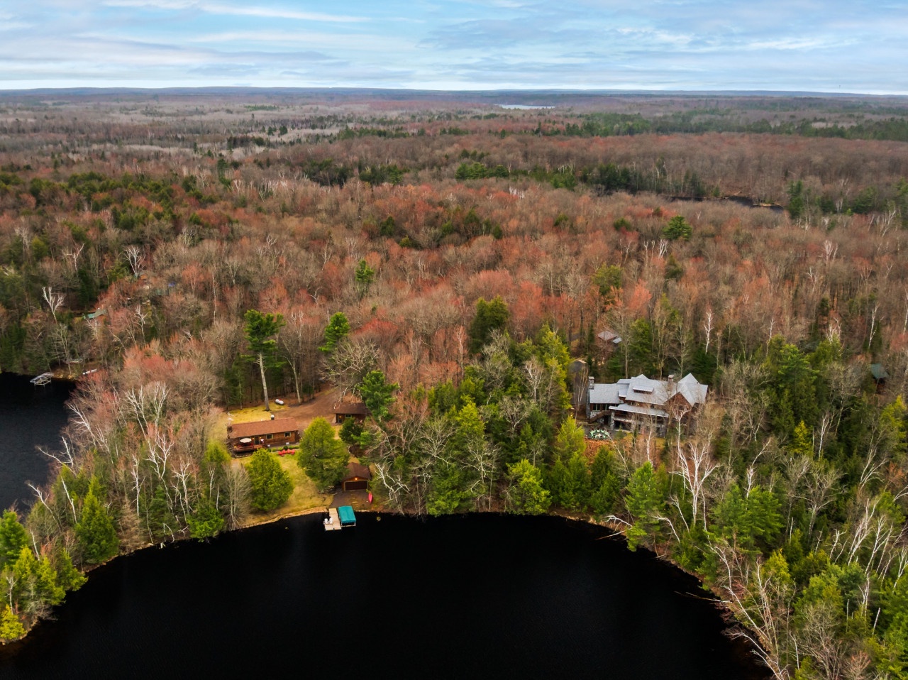 Aerial view of lakefront property nestled among vibrant autumn foliage with private dock and surrounding forest wilderness.