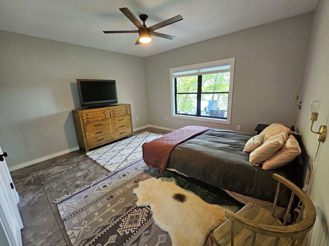 Your serene bedroom features a cozy bed, natural light from large windows, and modern amenities like a ceiling fan and TV for ultimate comfort.