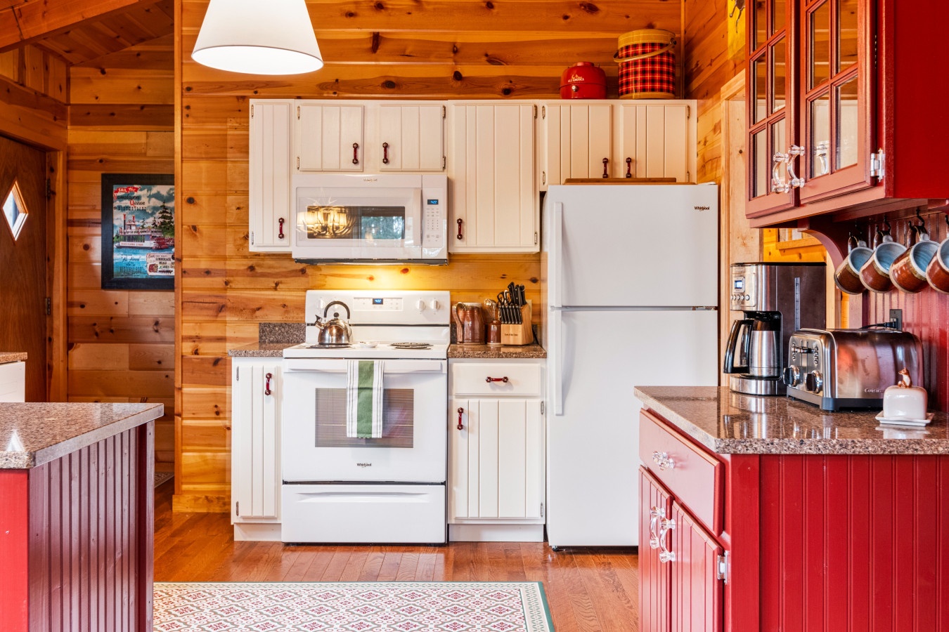 Your cozy cabin kitchen blends rustic charm with modern convenience, featuring warm wood walls and vibrant red cabinetry for memorable meal prep.