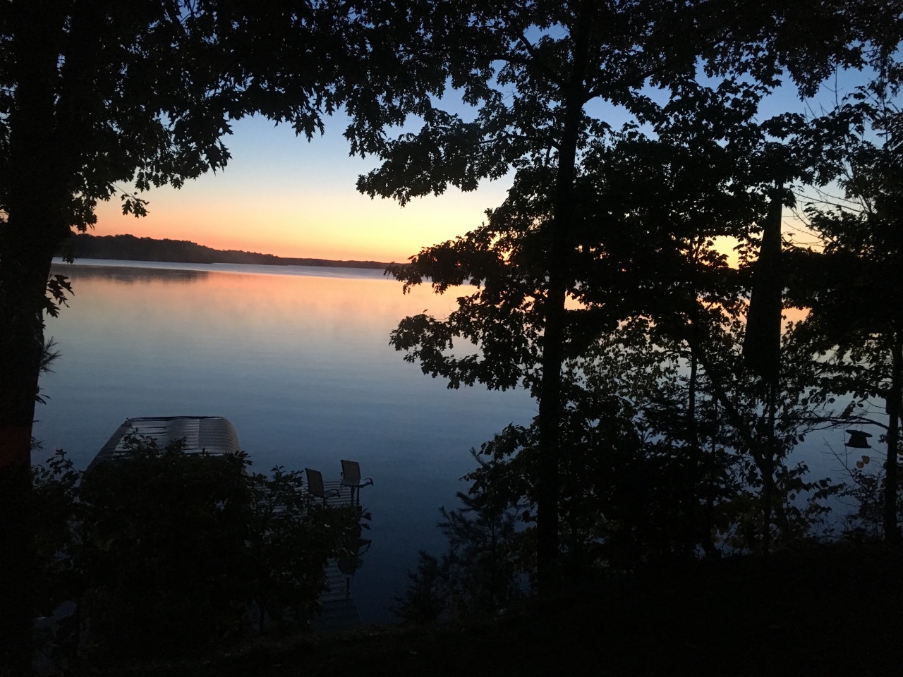 Tranquil lakefront setting with a private dock framed by mature trees, perfect for peaceful sunset moments.