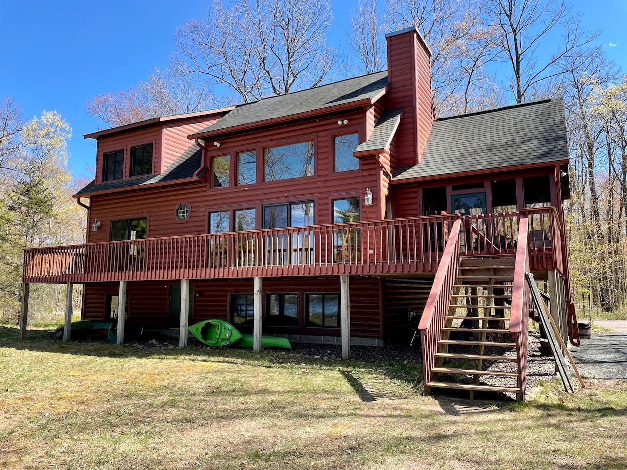Charming red cedar cabin nestled among bare trees with spacious deck and kayak storage for outdoor adventures.