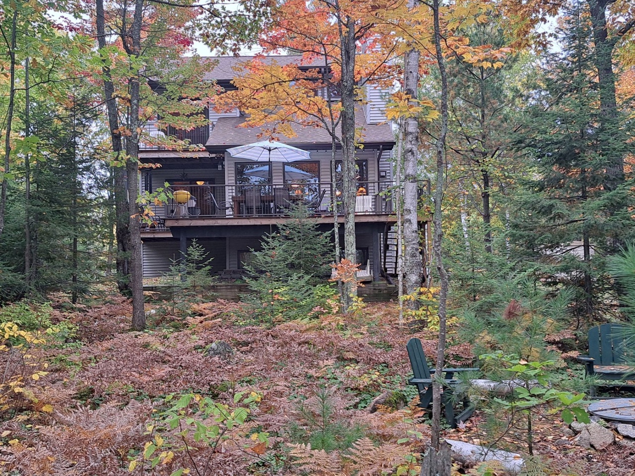 A beautiful two-story lakeside retreat nestled among vibrant autumn trees, featuring a spacious deck perfect for seasonal relaxation.