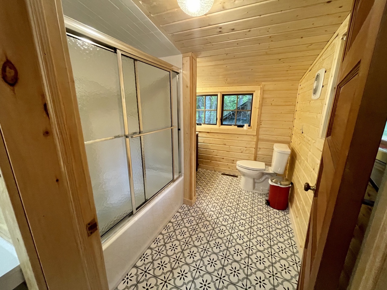 Relax in your spacious bathroom featuring warm wood walls, a sliding glass shower, and charming patterned tiles that add rustic elegance to your stay.