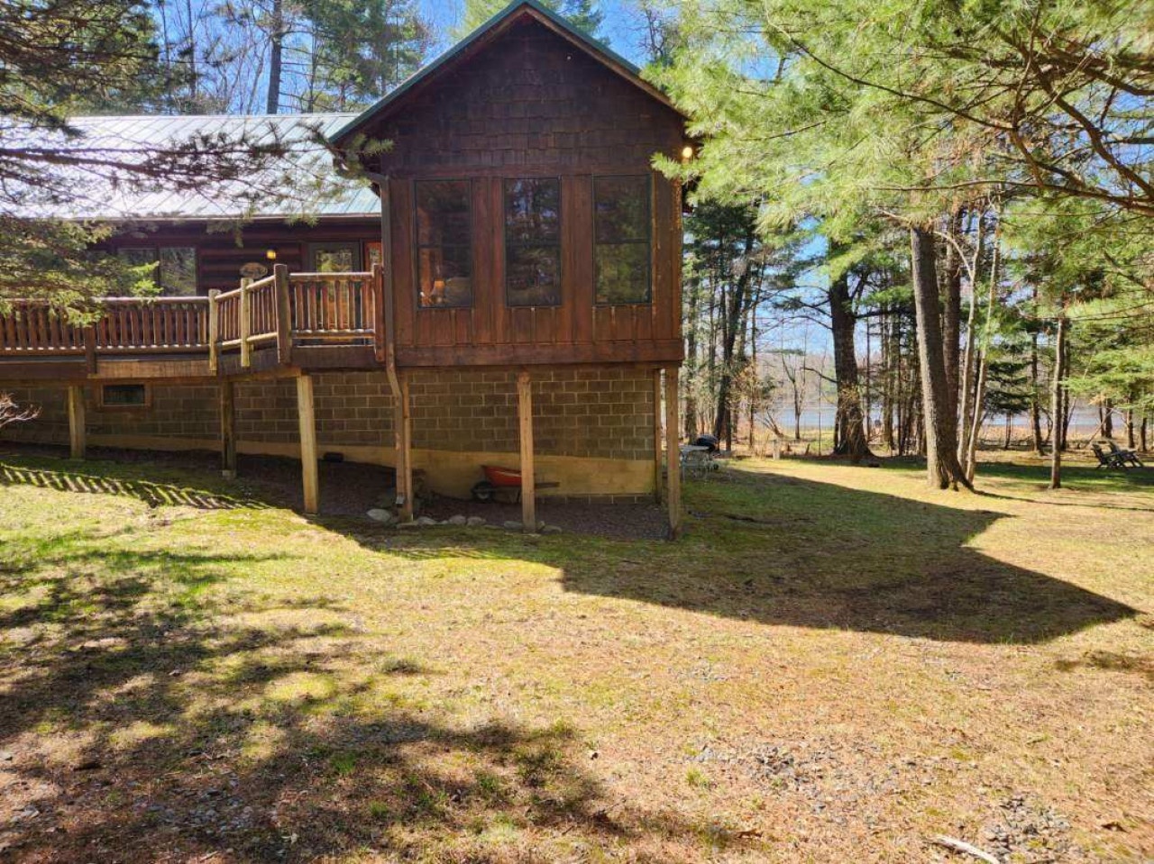 Charming woodland cabin with wrap-around deck nestled among towering trees, featuring rustic stone foundation and peaceful forest setting.