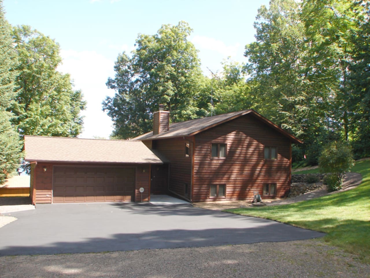 A charming cedar-sided retreat nestled among towering trees, featuring a spacious driveway and peaceful wooded surroundings for your forest getaway.