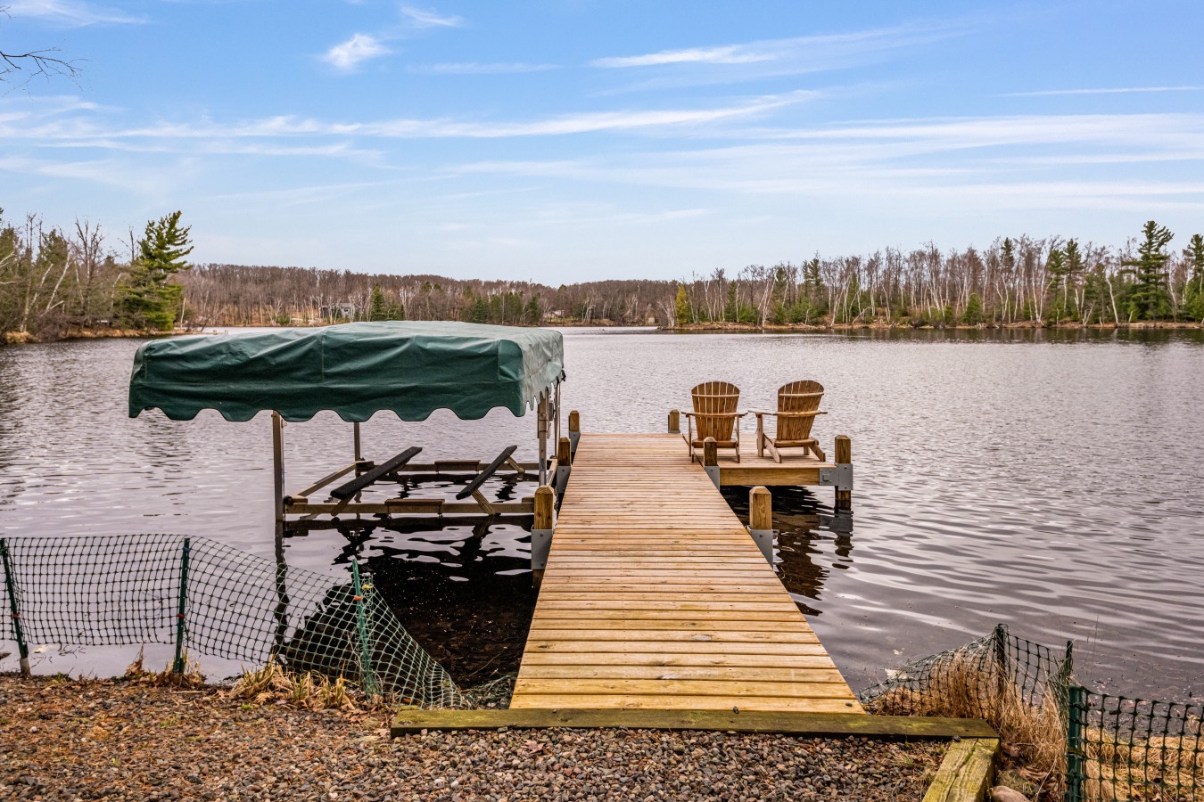 Waterfront dock with Adirondack chairs overlooking a serene lake surrounded by forest.