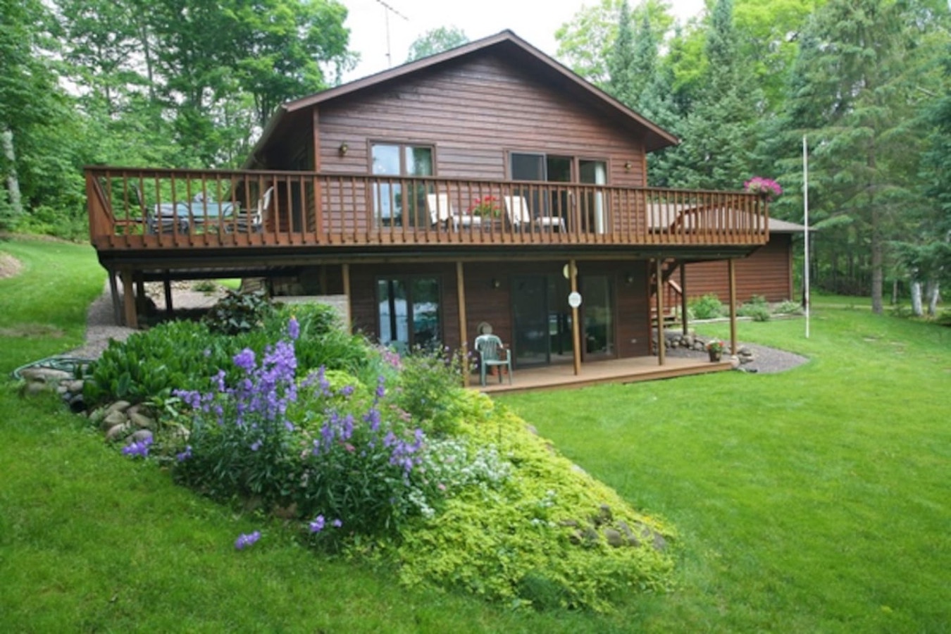 Charming wooden lodge surrounded by lush green lawns and mature trees in a peaceful natural setting.