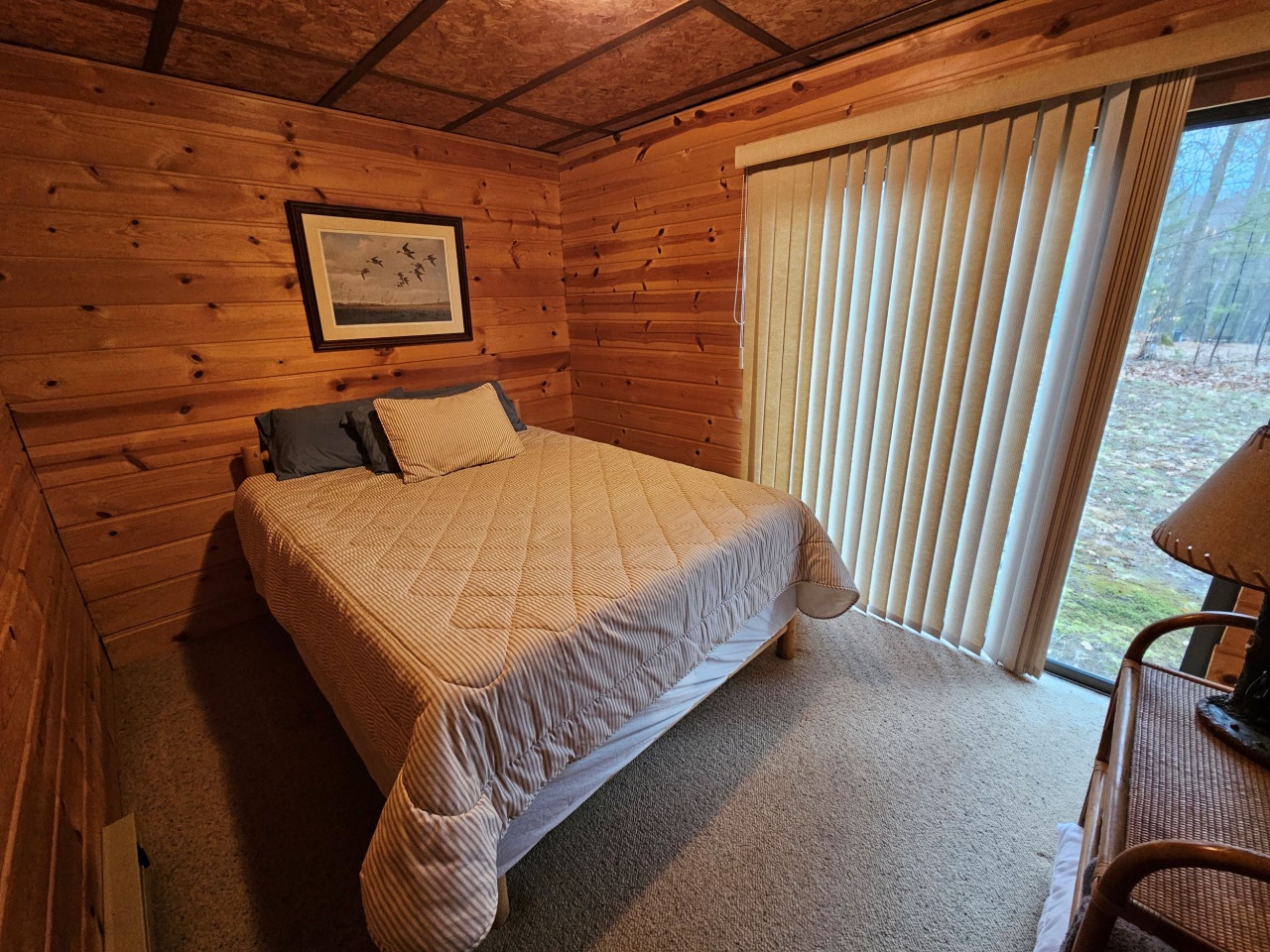 Wake up surrounded by warm wood walls in this cozy bedroom, where natural light streams through large windows overlooking peaceful grounds.