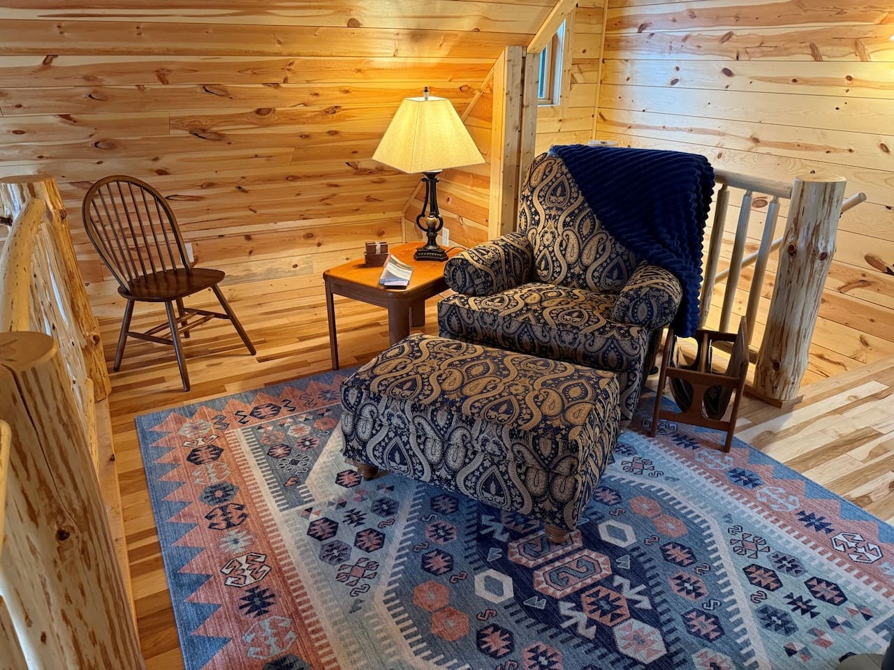 Sink into this cozy paisley armchair beside warm wood walls, where soft lamplight creates your perfect reading nook.